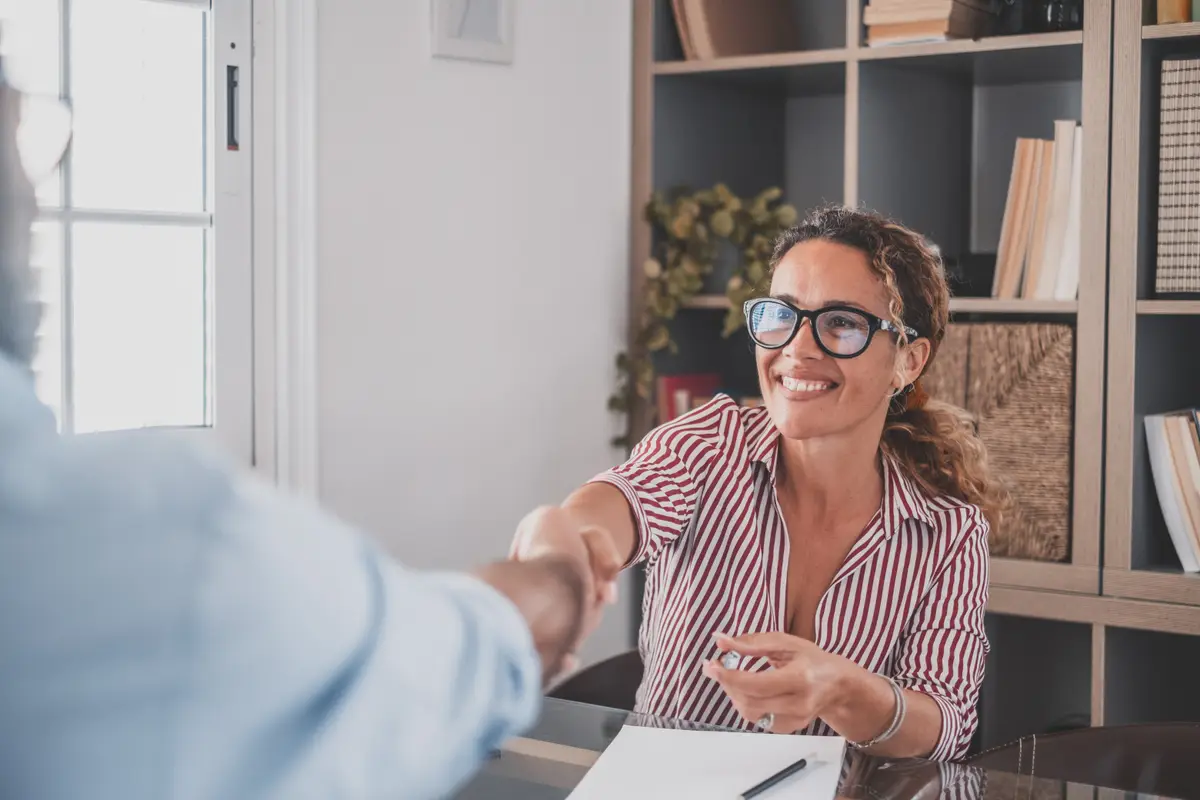 An agent shaking hands with a client across a desk